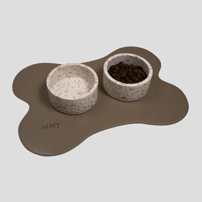 Two speckled ceramic dog bowls on a bone-shaped taupe placemat