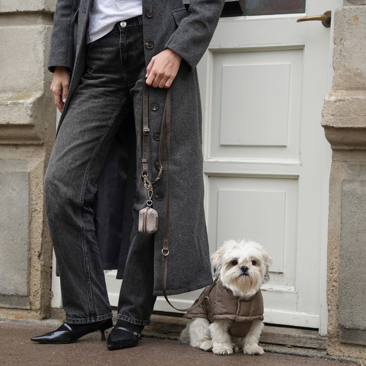 Shih tzu na smyczy, w pikowanym płaszczyku w kolorze Taupe, stojące obok swojego właściciela