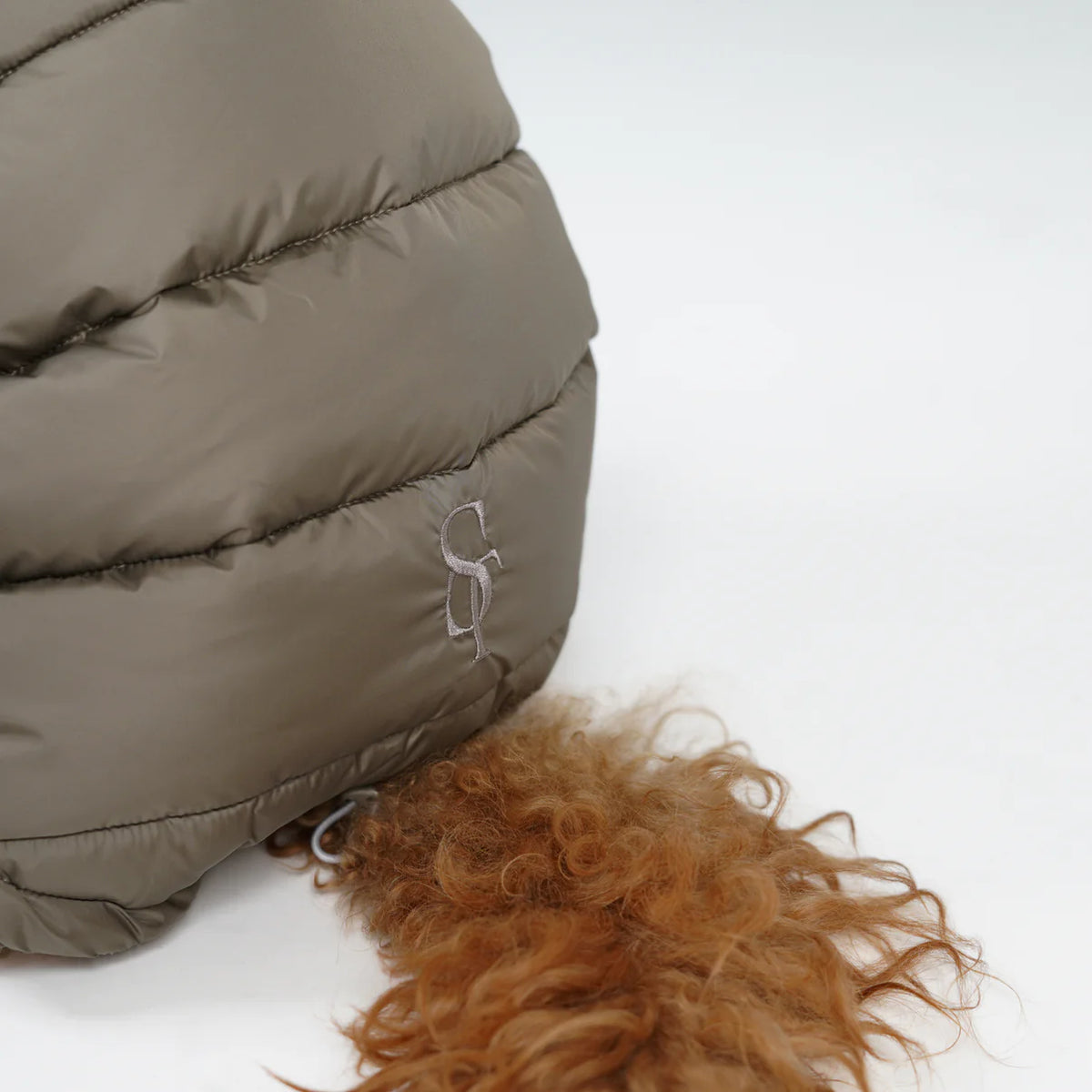 Zbliżenie na wytłoczony monogram „Staey” na pikowanym płaszczu w kolorze Taupe