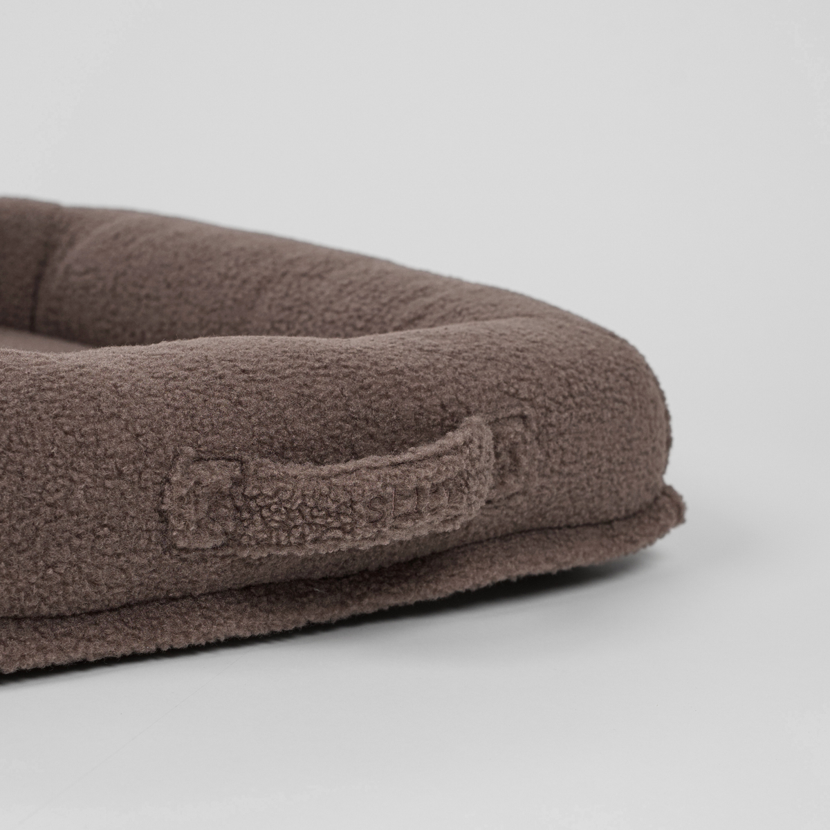 Close-up of the carry handle on the taupe teddy dog bed